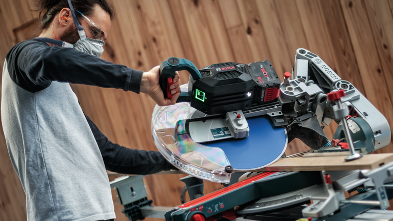 車間裡，配戴安全設備的人員使用圓鋸切割木材。.