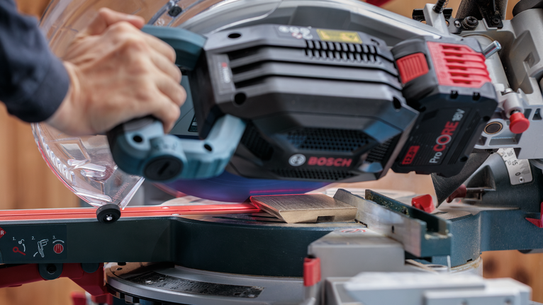 一名人員引導滑動斜切鋸穿過木板。.