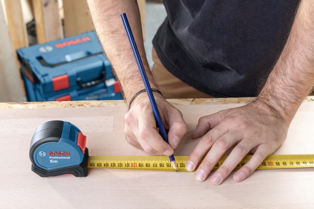 有人用捲尺和鉛筆在木頭上做測量標記。