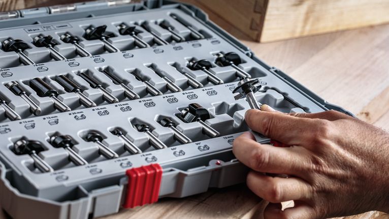 人們從木質表面上整齊排列的工具箱中挑選路由器鑽頭。.