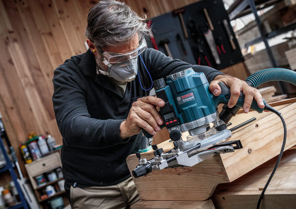 配戴安全設備的人員使用路由器來塑造木板的邊緣。.
