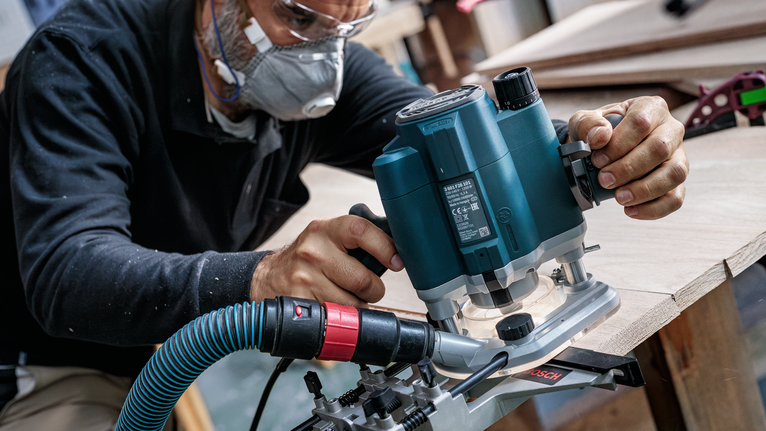 佩戴安全設備的人員使用電動銑刀來修整木板的邊緣。.