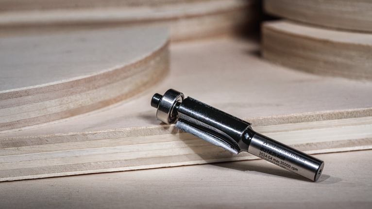 路由器鑽頭放置在堆疊的膠合板附近的木質表面上。.