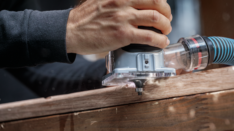 人員引導電動銑刀沿著木板進行精確的邊緣修整。.