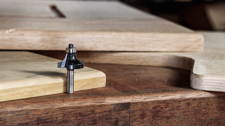 路由器鑽頭放在木製工作台上，旁邊是切割成型的木板。.