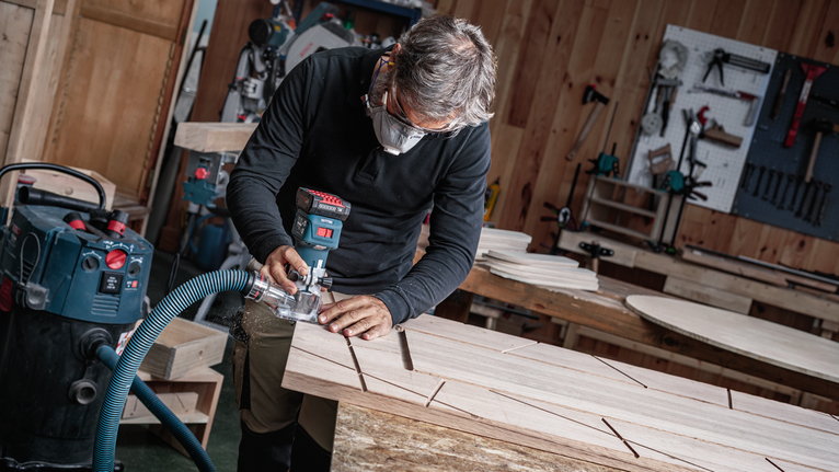 配戴安全設備的人員使用電動工具在木板上開槽。.