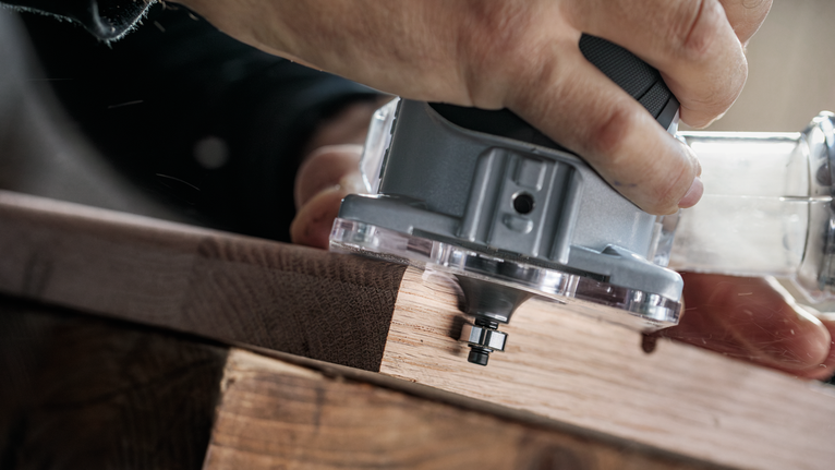 一名男子正操作電動修邊機沿著木板邊緣修整。.