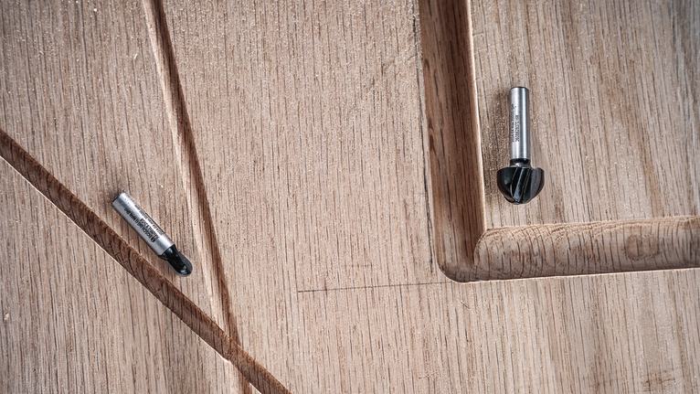 兩個路由器鑽頭放在帶有凹槽細節的雕刻木質表面上。.