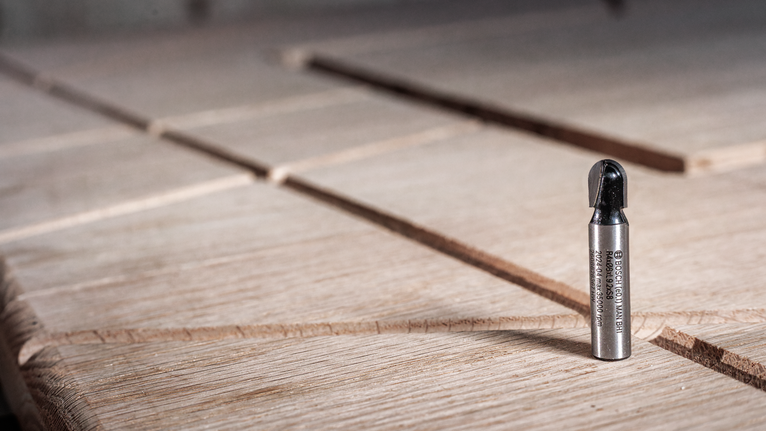 金屬路由器鑽頭直立在有凹槽的木質表面上。.