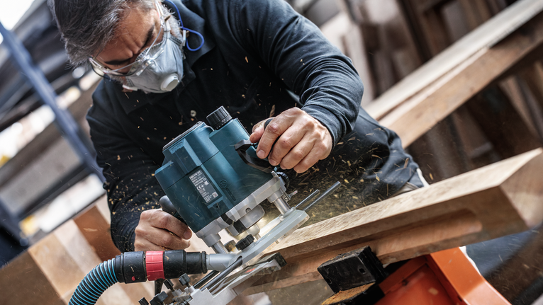 佩戴安全設備的人員使用電動銑刀修整木材。.