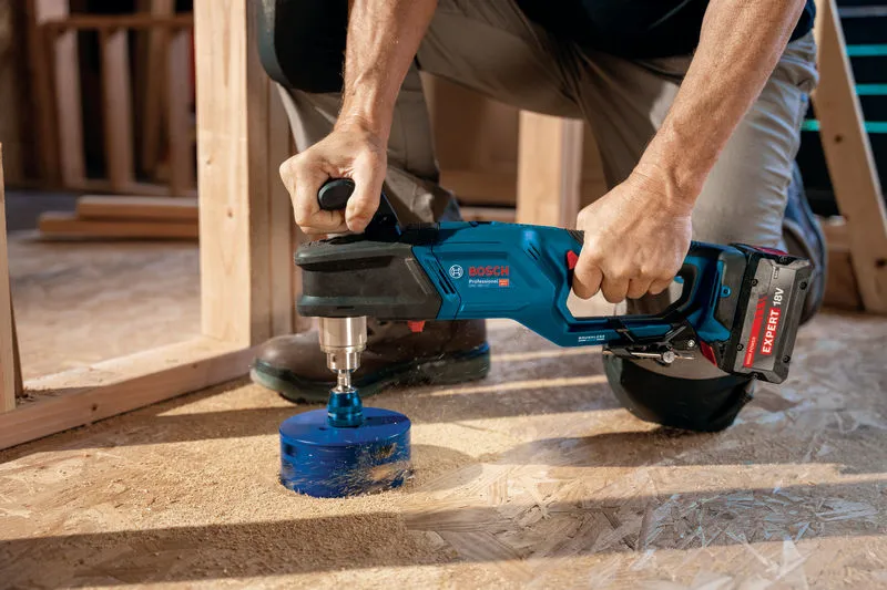 一個人使用無線角鑽在木地板上鑽了一個大洞。.