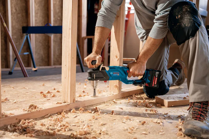 一名配戴安全設備的人員使用無線角鑽對木框架進行鑽孔。.