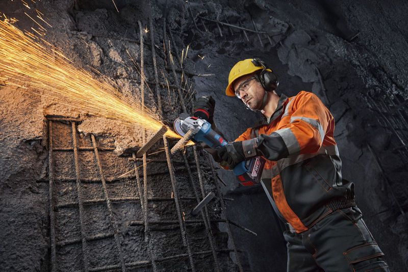 一名穿戴安全裝備的人員使用角磨機切割鋼筋，產生火花。