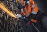 一名穿戴安全裝備的工人正在使用角磨機切割鋼筋。