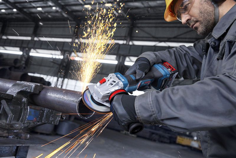 一名穿戴安全裝備的人員用角磨機打磨金屬管，產生火花。