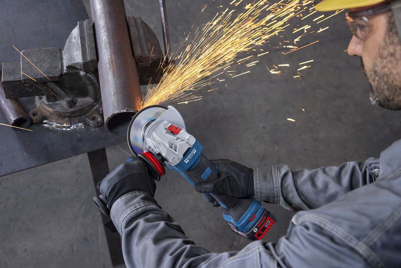 一名穿戴安全裝備的人員正在使用角磨機切割金屬管。