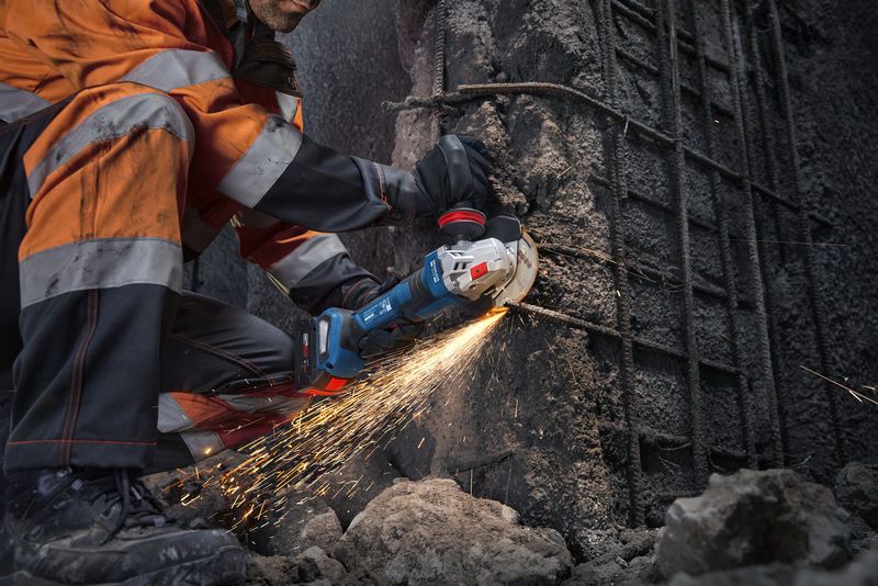 一名穿戴安全裝備的人員使用角磨機切割混凝土，產生火花。