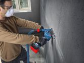 一名穿戴安全裝備的人員使用角磨機在混凝土牆上切割凹槽。