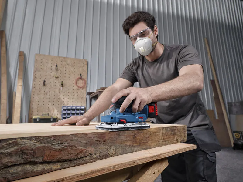 一名配戴安全裝備的人員正在使用無線軌道砂光機打磨木板。.