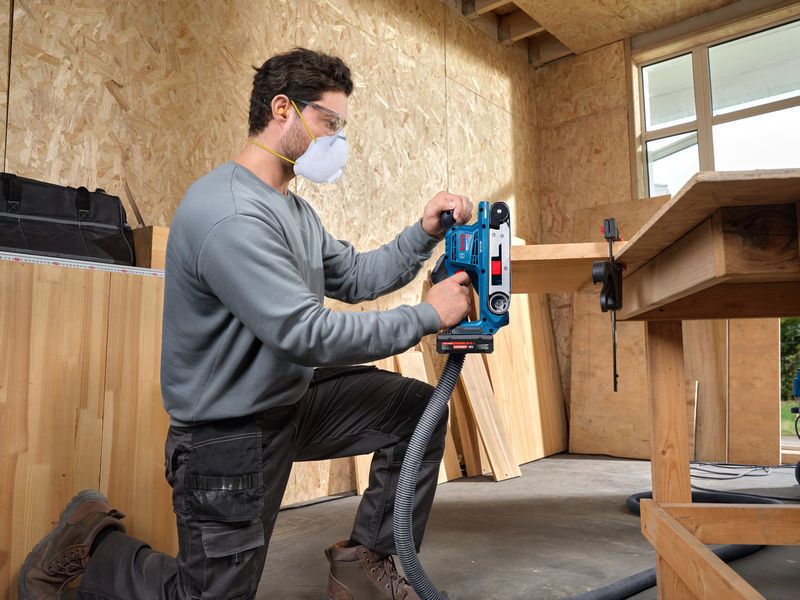 一名穿戴安全裝備的人員正在使用帶式砂光機打磨木板。