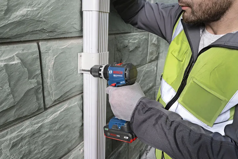 一名穿戴安全裝備的人員使用無線電鑽將支架固定在牆上。