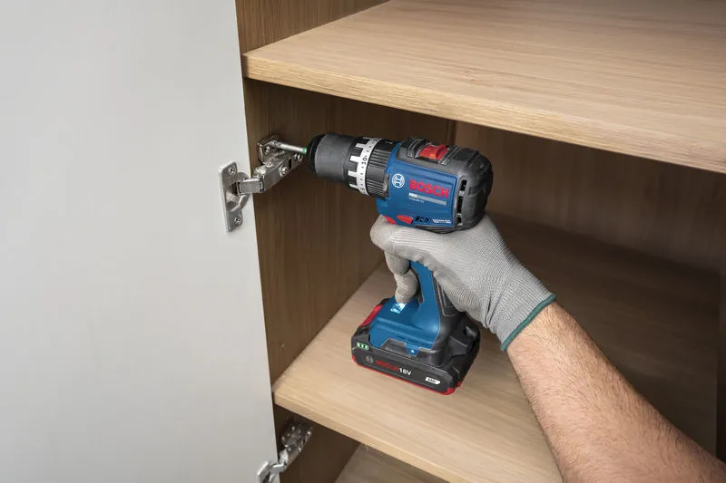 一名佩戴安全裝備的人員使用無線衝擊鑽安裝櫥櫃鉸鏈。