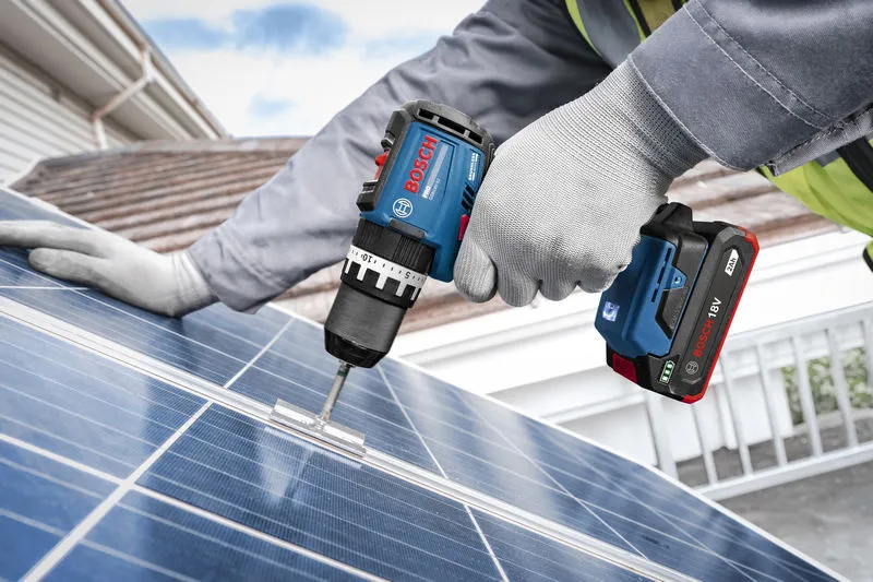 一名穿戴安全裝備的人員使用無線衝擊鑽將支架固定在太陽能板上。