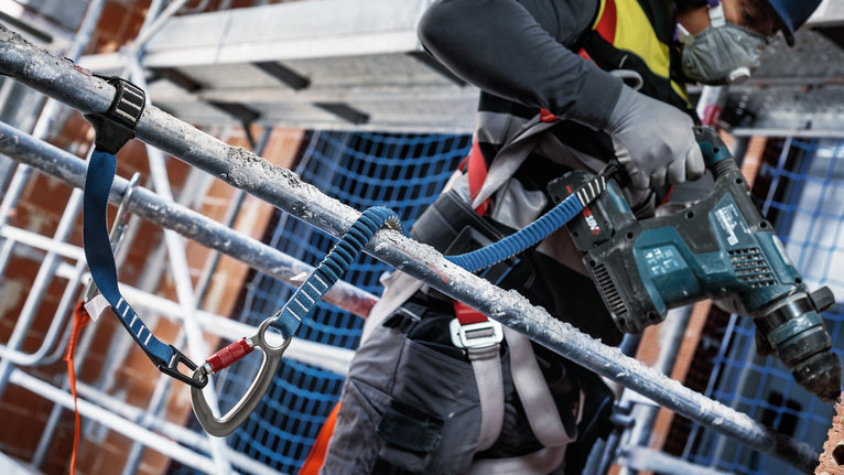 配戴安全設備的人員在鷹架上鑽入混凝土。.