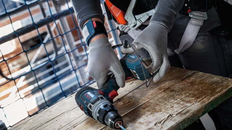 配戴安全設備的人員在木質工作檯面上調整無線電鑽。.