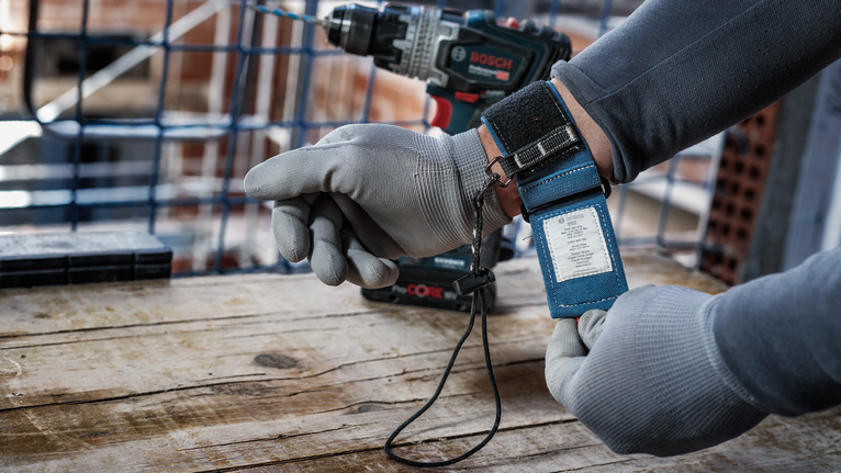 配戴安全設備的人員在木質表面上的無線電鑽附近調整腕帶。.