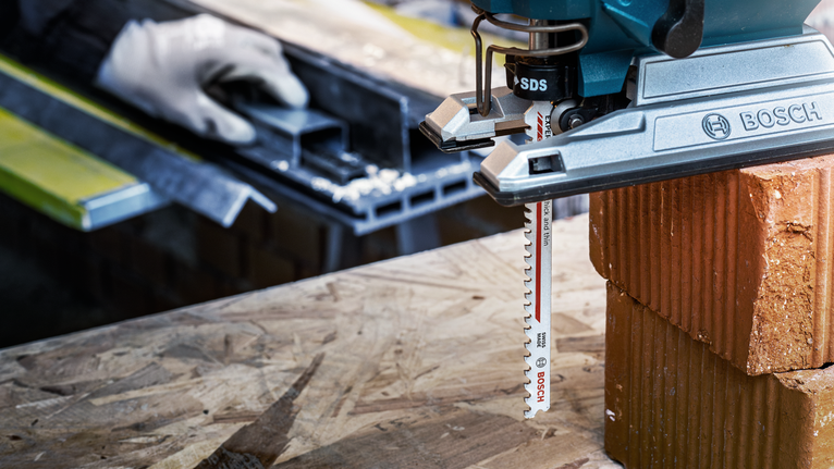 配戴安全設備的人使用曲線鋸在木質表面上切割磚塊。.