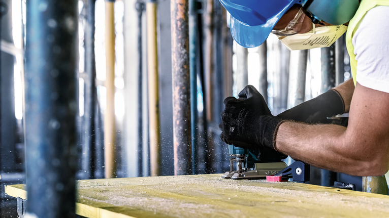 配戴安全設備的人員使用電動工具切割木材。.