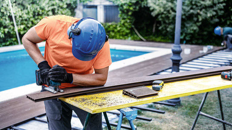 配戴安全裝備的人員使用曲線鋸在戶外切割甲板板。.