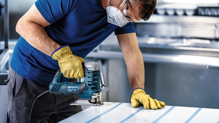 配戴安全設備的人員使用曲線鋸切割金屬板。.