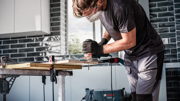 配戴安全設備的人員使用曲線鋸在工作台上切割木材。.