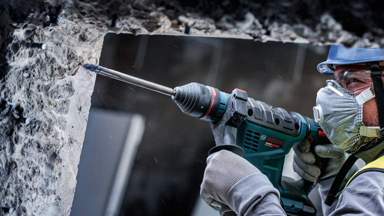 一名配戴安全設備的人員使用旋轉錘在混凝土牆上鑽孔。