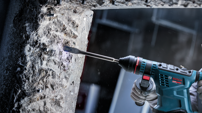 配戴安全設備的人員使用電動工具鑿混凝土。