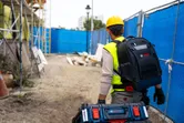 一名身穿安全裝備的人員在建築工地背著承包商背包和行李箱系統。