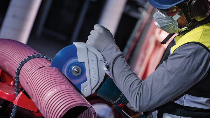 一名配戴安全設備的人員正在用電動切割機切割一根大型塑膠管。