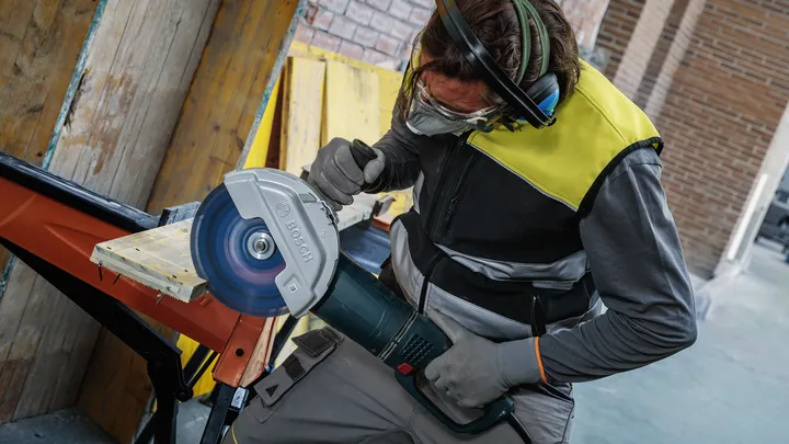 配戴安全設備的人員用大型圓鋸切割木板。