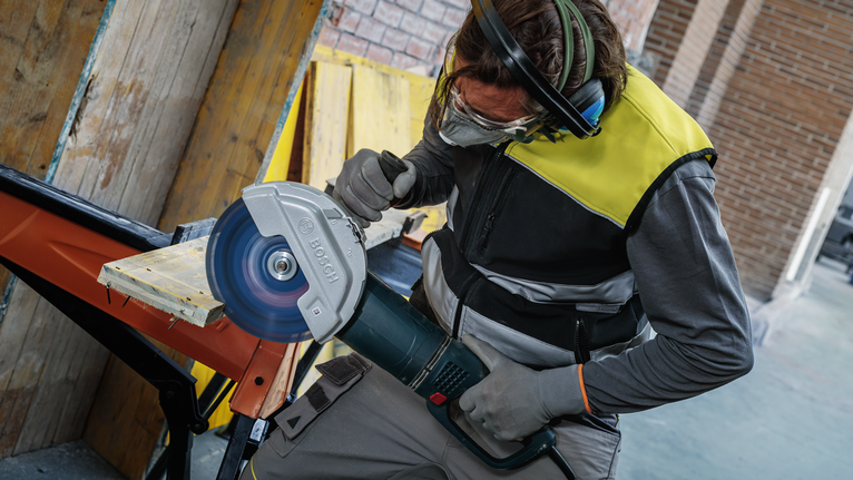 配戴安全設備的人員用大型圓鋸切割木板。