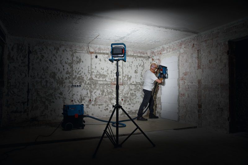 一名配戴安全設備的人員在工作燈下操作牆壁鑽孔工具。