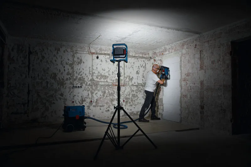 一名配戴安全設備的人員在工作燈下操作牆壁鑽孔工具。