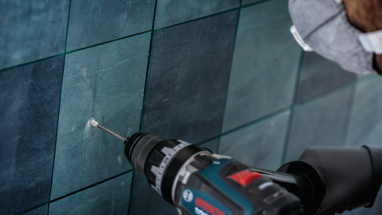 配戴安全設備的人員在磁磚牆上鑽孔。