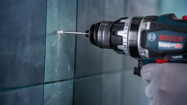 佩戴安全設備的人員正在向瓷磚牆上鑽孔。