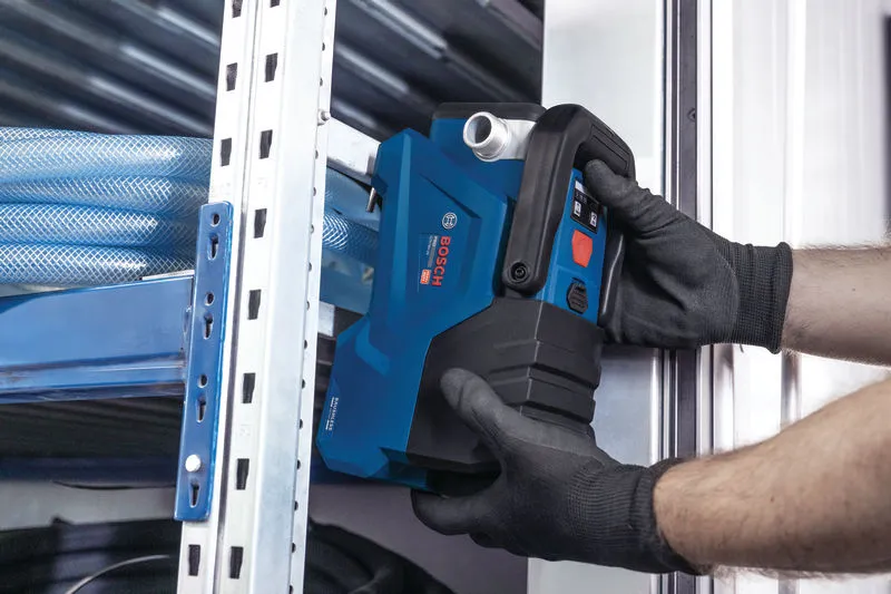 一名穿戴安全裝備的人員正在金屬貨架附近安裝一台藍色電動工具。