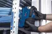 一名穿戴安全裝備的人員正在金屬貨架附近安裝一台藍色電動工具。