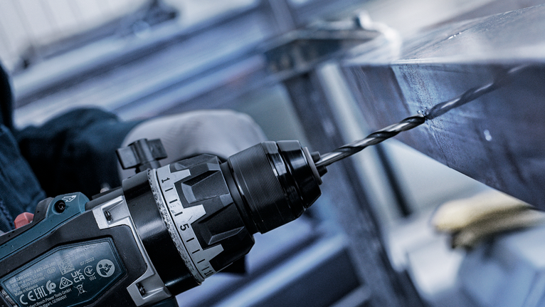 一名穿戴安全裝備的人員正在金屬樑上鑽孔。