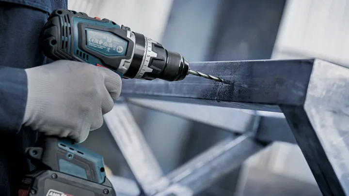 一名穿戴安全裝備的人員正在金屬樑上鑽孔。