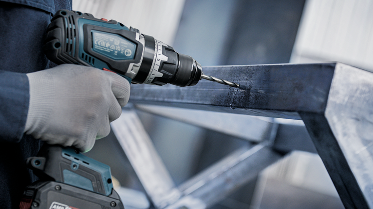 一名穿戴安全裝備的人員正在金屬樑上鑽孔。